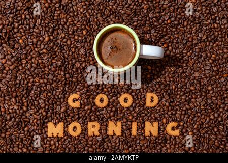 White cafe Tasse und Worte GUTEN MORGEN aus Keks Buchstaben auf einem dunklen Kaffeebohne background-image Stockfoto