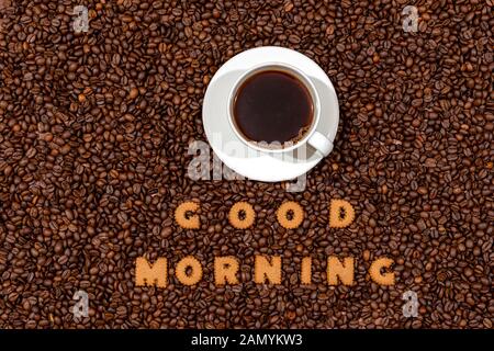 White cafe Tasse und Worte GUTEN MORGEN aus Keks Buchstaben auf einem dunklen Kaffeebohne background-image Stockfoto