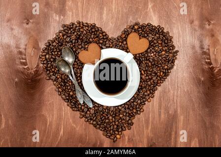 White Coffee Mug, herzförmige Honigkuchen und zwei Löffeln auf einem Sockel in Herzform aus Kaffeebohnen hergestellt - Bild Stockfoto