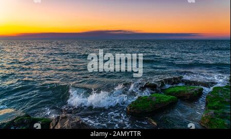 Wellen, die bei Sonnenuntergang auf der felsigen Küste abstürzen Stockfoto