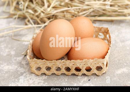 Frische braune Eier in einer Weidenschale isoliert. Stapel von rohem Hühnereier auf Reisstroh Hintergrund. Stockfoto