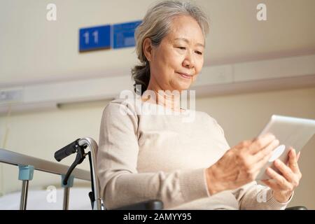 Asiatische Seniorin, die digitale Tablette in Pflegeheim oder auf der Krankenstation verwendet Stockfoto