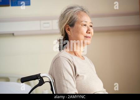 Inhalt asiatische ältere Frau sitzt im Rollstuhl in ihrem Zimmer im Pflegeheim mit ruhiger Gesichtsausdruck Stockfoto