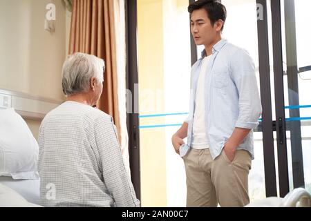 Junger asiatischer Erwachsener, der im Krankenhaus oder im Pflegeheim mit dem älteren Vater spricht Stockfoto