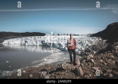 Ein junger Mann reisender Tourist vor Eqip Sermia Gletscher Eqi Gletscher genannt. Wand aus Eis im Hintergrund. Das Konzept der globalen Erwärmung und der Stockfoto