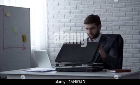 Mann im Anzug sitzt im Büro mit offenem Aktenkoffer und bereitet sich auf Geschäftsreise vor Stockfoto
