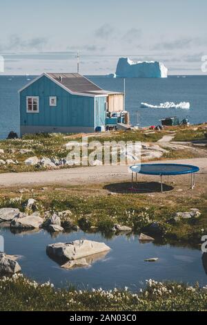 Typisches buntes Holzfisherhaus mit Eisberg in Qeqertarsuq, Disko-Bucht-Gebiet Grönland und Ilulissat. Typische Architektur im arktischen Kreis Stockfoto