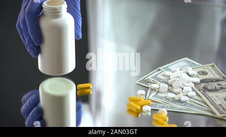 Hand halten Pillen Glas, fallen Tabletten auf Dollar, teure medizinische Behandlung Stockfoto