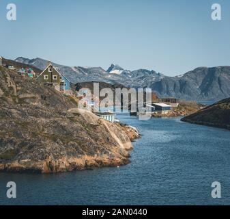 Bunte Häuser liegen an den hängen der Fischerstadt Kangaamiut, Westgrönland. Eisberge vom Kangia-Gletscher in Grönland schwimmen mit blauem Himmel Stockfoto