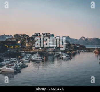 Blick auf den Sonnenuntergang über Maniitsoq arktische Stadt in Grönland. Berge im Hintergrund während der Mitternachtssonne. Farbenfrohe Häuser und Panorama. Ansicht zum Anschluss mit Stockfoto