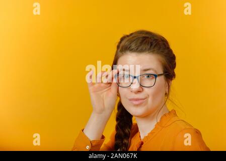 Mädchen mit Brille in die Kamera schaut auf gelbem Hintergrund. Stockfoto