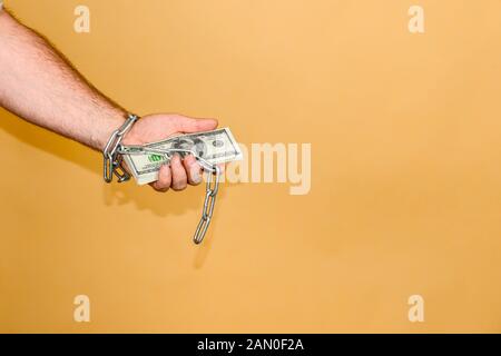 Der Mann ist in einer Kette umwickelt, hält Dollar. Das Konzept der monetären und finanziellen Abhängigkeit. Stockfoto