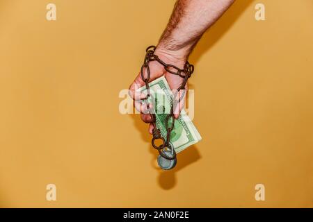 Der Mann ist in einer Kette umwickelt, hält Dollar. Das Konzept der monetären und finanziellen Abhängigkeit. Stockfoto