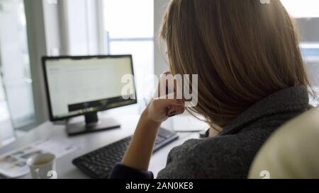 Überarbeiteter, im Büro sitzender Dame, der die Dokumentation liest und auf das Tagesende wartet Stockfoto