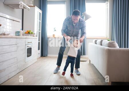 Kleines süßes Baby Mädchen, die ihre ersten Schritte mit vatis Hilfe Stockfoto