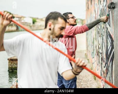 Zwei Autoren, die die Wand mit Farbe grau vor dem Lackieren ihre Bild - Zeitgenössische Künstler bei der Arbeit - Urban Lifestyle, Street Art Konzept-Foc Stockfoto