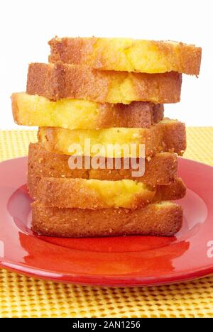 Ein Stapel gemachter Zitronenkuchen in Scheiben auf einem roten Teller. Der Hintergrund ist isoliert und enthält eine gelb strukturierte, karierte Kunststoff-Platzmatte. Stockfoto