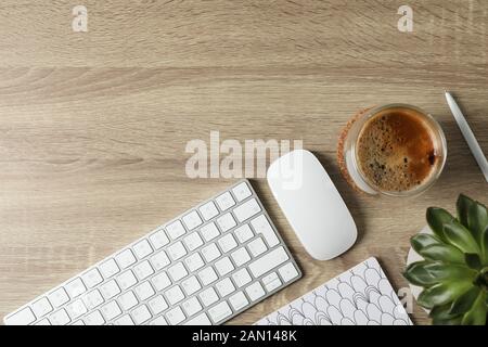 Arbeitsplatz. Tastatur, Maus, Glas Kaffee und Pflanzen auf Holztisch, Draufsicht Stockfoto