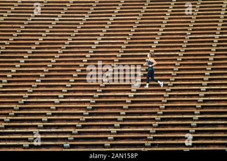 Frau jogging gegenüber Sitzreihen an Red Rocks Amphitheater entfernt in Morrison, Colorado, während Sie Musik hören auf dem Mobiltelefon Stockfoto