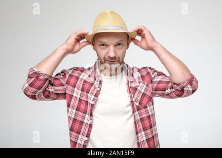 Kaukasischer Mann legt Hut und sieht unbestimmt auf die Kamera. Stockfoto