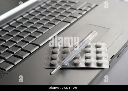 Pillen in Blister und Thermometer auf einer silbernen Tastatur. Stockfoto