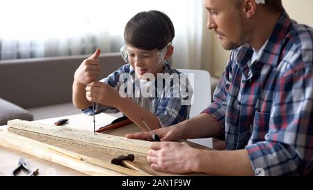 Vater unterrichte seinen lächelnden Sohn Zimmerei, der kleine Junge in der Werkstatt mit Screwer Stockfoto
