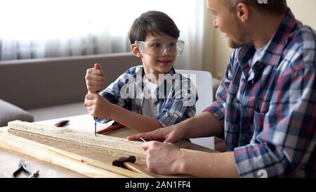 Daddy unterrichte seinen lächelnden Sohn Zimmerei, den kleinen Jungen mit Screwer in der Werkstatt Stockfoto
