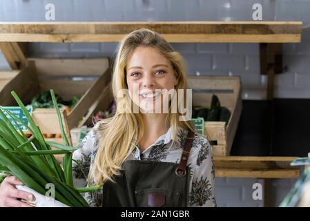 Lächelnde junge Frau, die Frühlingszwiebel im Korbkorb hält Stockfoto