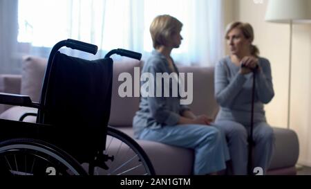 Fürsorgliche Tochter im Gespräch mit behinderten älteren Mutter zu Hause, Rehabilitation Stockfoto