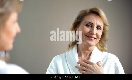 Attraktive Seniorin, die Spiegelbild und lächelnde, alter-Schönheit betrachtet Stockfoto