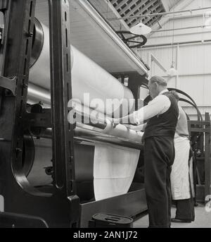 1950er Jahre, historische, Textilindustrie, ein männlicher Arbeiter in einer Weste an einer Stahlkonstruktion mit großen Rollen von Bettwäsche, Nordirland. Stockfoto