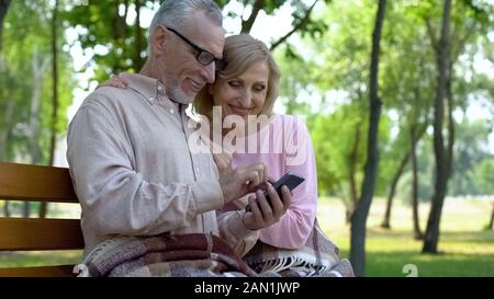 Gerne ältere Paare, Kinder online, draußen sitzen, Smartphone App Stockfoto