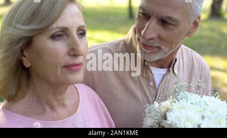 Grauhaarige Rentner Mann mit weißen Blumen auf attraktive ältere Frau Stockfoto