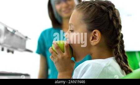 Junges Mädchen beißen Apple in Zahnmedizin, Zahnarzt lächelnd im Hintergrund Stockfoto