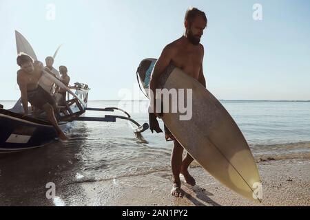 Erwachsene Männer tragen Surfbretter beim Entladen des Schiffes Stockfoto