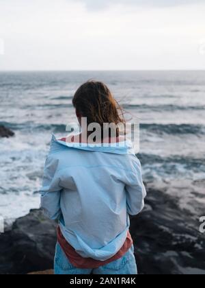 Junge Frau, die auf den Ozean schaut Stockfoto