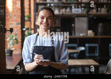 Porträt einer lächelnden Kellnerin in der Schürze mit Blick auf die Kamera Stockfoto