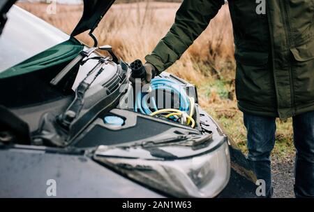 Mann, der ein Elektroauto-Kabel in die Motorhaube des Autos führt Stockfoto