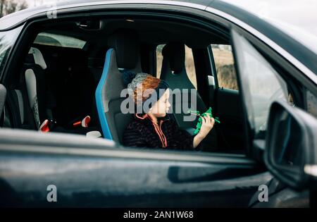 Der junge Junge saß in einem Elektroauto und spielte mit Spielzeug Stockfoto