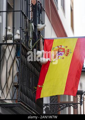 Eine Sammlung gegossener Tauben blickt auf eine spanische Flagge, die von einem traditionellen, schmiedeeisernen Balkon aus Sevilla mit Mannequin's Legs & Men's Krawatten hängt. Stockfoto