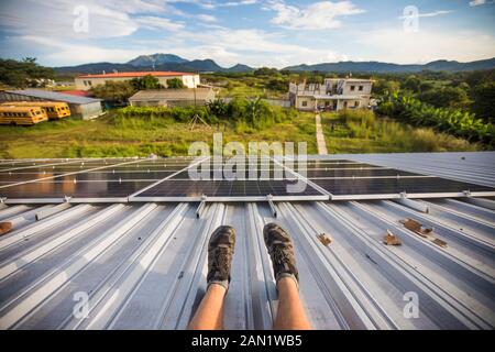 Hohe Winkelansicht der Beine der Arbeiter und installierte Solarpaneele vom Dach. Stockfoto