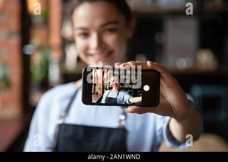 Lächelnde Kellnerin hält Handy, die selfie im Restaurant macht Stockfoto