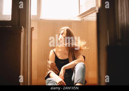 Junge Frau wirft Haare, während sie auf dem Boden auf dem Balkon zu Hause sitzen Stockfoto