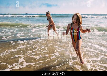 Schwestern, die am Strand laufen und im Wasser planschen Stockfoto