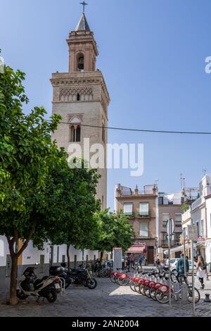 Eine Reihe von Sevici mietet Fahrräder, die in der Calle Vergara im Schatten des 22 m hohen Glockenturms von Vermondo Resta für die Iglesia de San Marcos geparkt sind Stockfoto