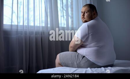 Traurig fetter Mann auf dem Bett, zu Hause zu sitzen, an der Kamera, Depression, Unsicherheit Stockfoto