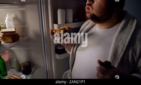 Beleibte Bachelor essen Pizza in der Nähe von Kühlschrank, Bier, ungesunden Lebensstil Stockfoto