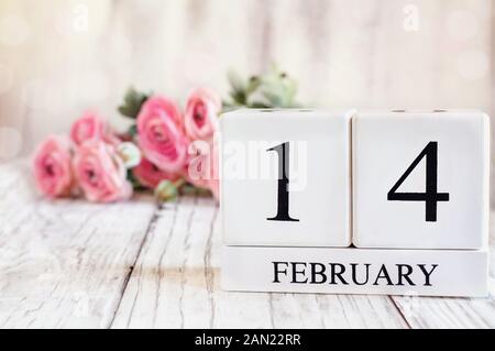 Weißes Holz Kalender Blöcke mit dem Datum 14. Februar für Valentines Tag. Selektiver Fokus mit rosa Ranunkeln über einen hölzernen Tisch. Stockfoto