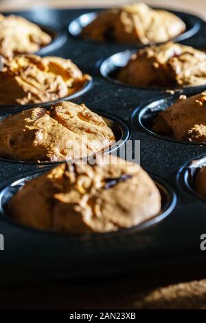 Close-up auf eine Reihe von leckeren veganen Schoko Vanille Muffins in einem schwarzen Muffin Pan im Sonnenlicht - Blick diagonal, vertikal Hochformat Stockfoto