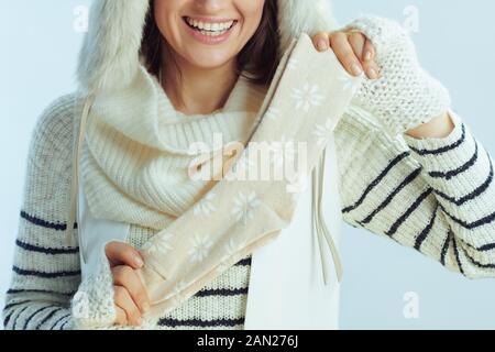 Nahaufnahme von fröhlicher eleganter Frau in weiß gestreiftem Pullover, Schal und Ohrenklappenhut mit Wintersocken vor hellblauem Hintergrund. Stockfoto